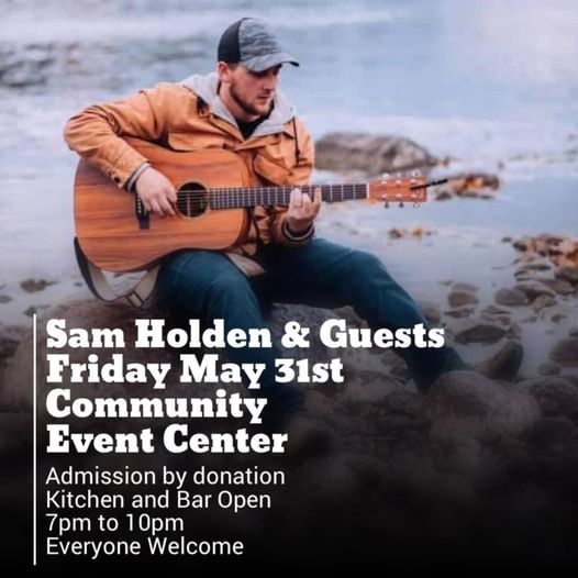 Sam Holden sitting on lake shore rocks, playing a guitar.